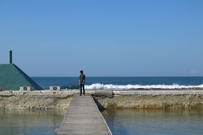 Rear view of man standing on pier at beach