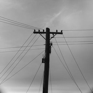 Low angle view of electricity pylon against cloudy sky