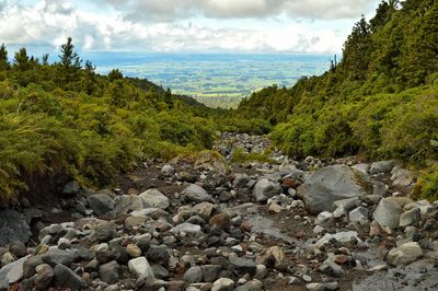 Rocks by river against cloudy sky