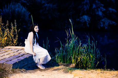 Young woman sitting by pond at night