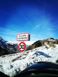 Road sign on snow covered mountain against blue sky