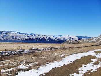 Scenic view of snowcapped field against clear blue sky