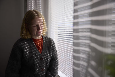 Pensive teenage girl looking through window