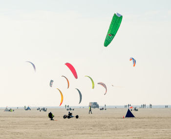 Multi colored parachutes fling over beach against clear sky