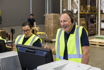 Confident senior male customer service representative talking through headset while standing by coworker in distribution