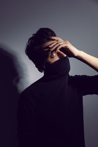 Fashion portrait man standing over a light gray background in a black sweater covers his face