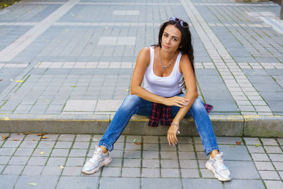 Happy young fashion woman sitting on the street sidewalk stylish female model