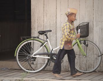 Full length of boy walking by bicycle on sidewalk