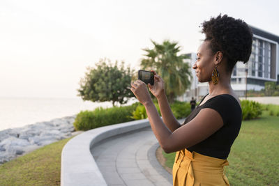 Smiling woman taking photo using smart phone at promenade