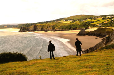 Rear view of people standing by cliff against beach and sky