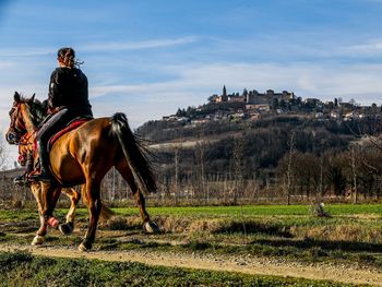 Woman riding horse on field against sky