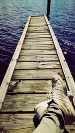 Low section of man sitting on pier at lake