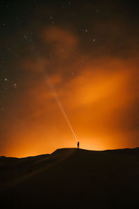 Silhouette person on land against sky during sunset in the desert full of stars