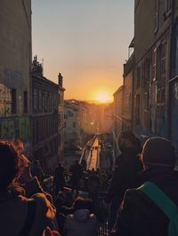 People on street amidst buildings in city during sunset