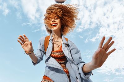 Young woman with arms raised standing against sky