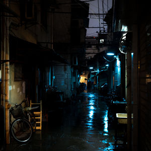 Wet street amidst illuminated buildings in city during rainy season