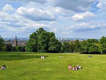 People and trees in queen's park against cloudy sky