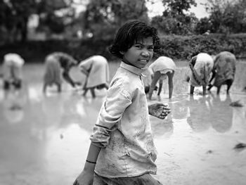 Portrait of boy standing against farmers harvesting rice paddy