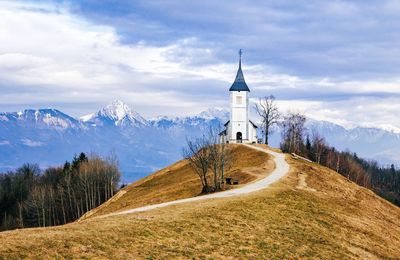 Scenic view of snowcapped mountains against sky. church on top of a hill, road, path.