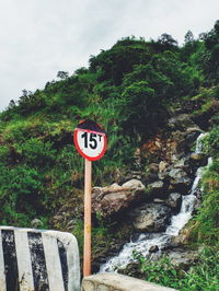 Road sign by trees against sky