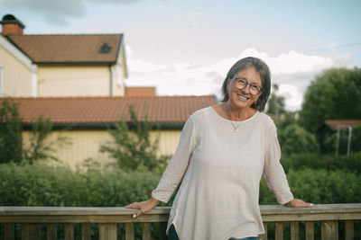 Portrait of senior woman standing against railing at porch