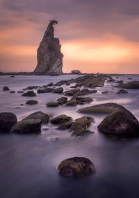 Rocks on sea shore against sky during sunset