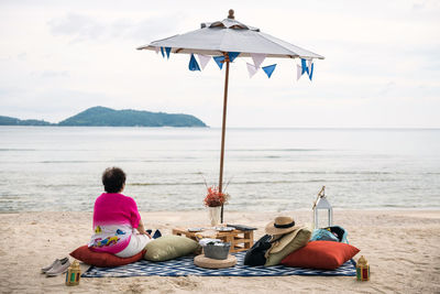 Old pension woman sit on beach picnic to drink, eat, and enjoy seascape view at beach in phuket