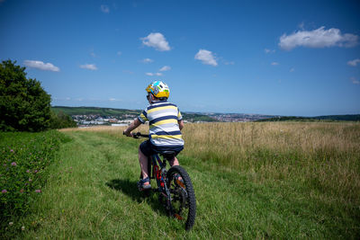 Rear view of man riding bicycle on field against sky