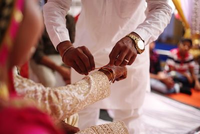 Midsection of man tying thread on groom hand