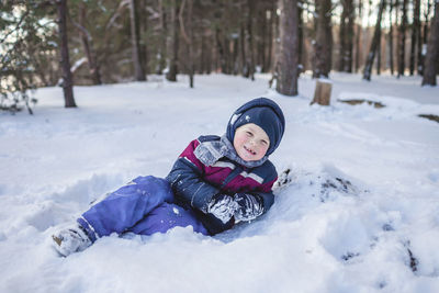 Happy boy enjoys winter season and lies in the snow in forest on sunny winter day. lovely winter