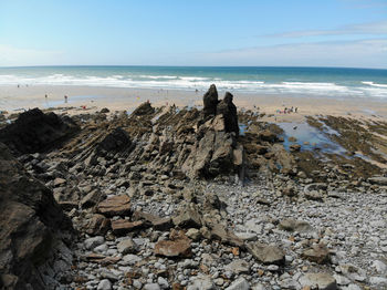 People on rocks at beach against sky