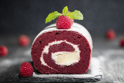 Red velvet sponge swiss roll with fresh raspberry and sugar icing on dark background