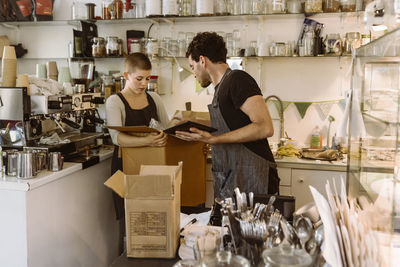 Side view of male owner assisting female colleague holding cardboard box at cafe