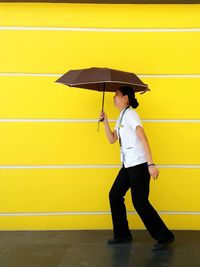 Side view of man holding yellow umbrella against wall