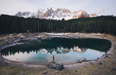 Man standing on rock by lake against snow covered mountains