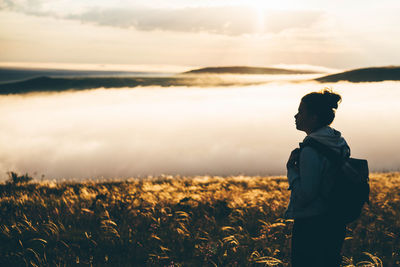 Rear view of man standing on field against sky during sunset