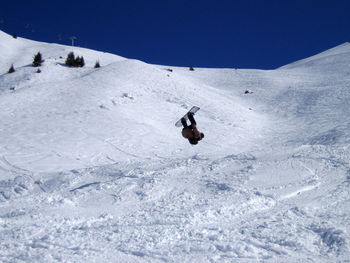 Man snowboarding on snowy field against clear blue sky during winter season