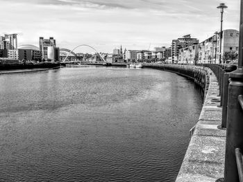 Bridge over river by buildings in city against sky