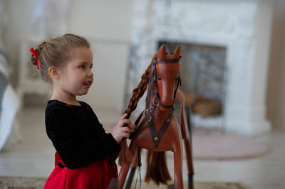 Beautiful little girl with a toy wooden horse in a vintage studio.