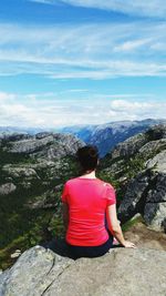 Rear view of man sitting on mountain against sky