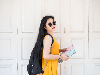 Young woman wearing sunglasses standing against door