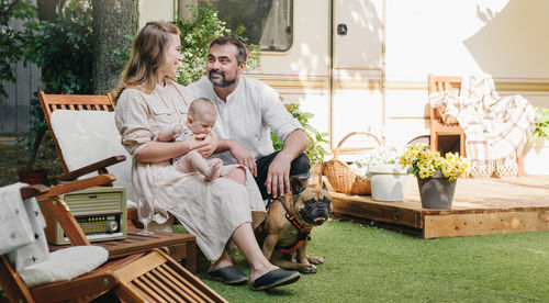 Family with baby and dog spending happy time together near trailer outside on deck chair, traveling