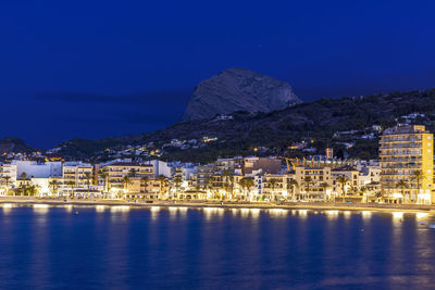 Illuminated buildings by sea against sky at night