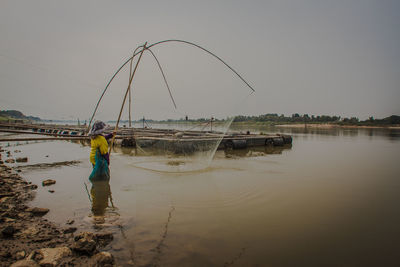 Rear view of man fishing in river against clear sky