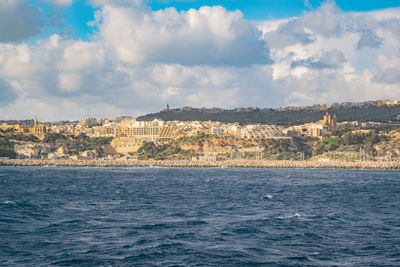 Scenic view of sea by townscape against sky