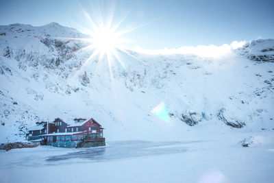 Scenic view of snow covered houses by mountain against sky in a sunny day on a frozen lake