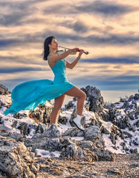Tanya is playing on violin on rock against sky during sunset