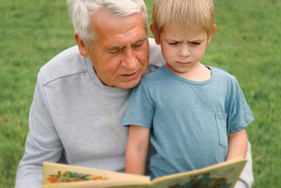 Happy grandfather reading book to curious grandson outdoors. close up. grandpa with grandchild