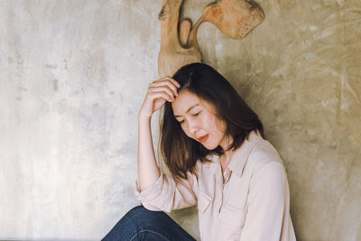 Beautiful young woman sitting against wall