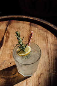 Rosemary lemonade soda cocktail with ice and picnic gingham drinking straw on whiskey barrel 